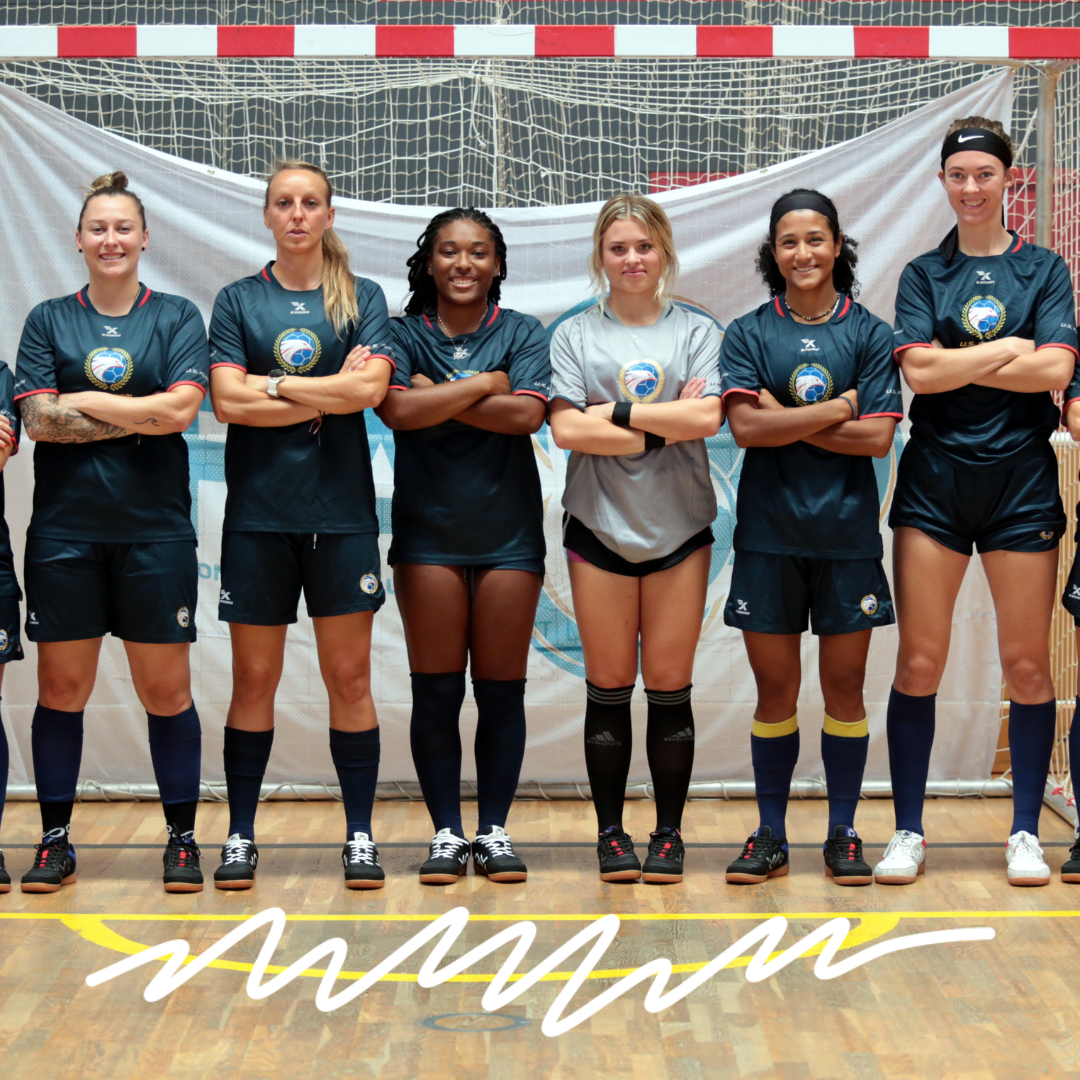 Photo of female futsal players standing in a line on a futsal court with arms crossed and smiling.