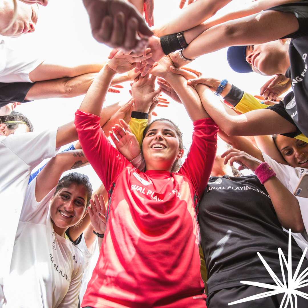 Photo looking from inside a huddle of female footballers smiling with their hands all in the middle of the circle.