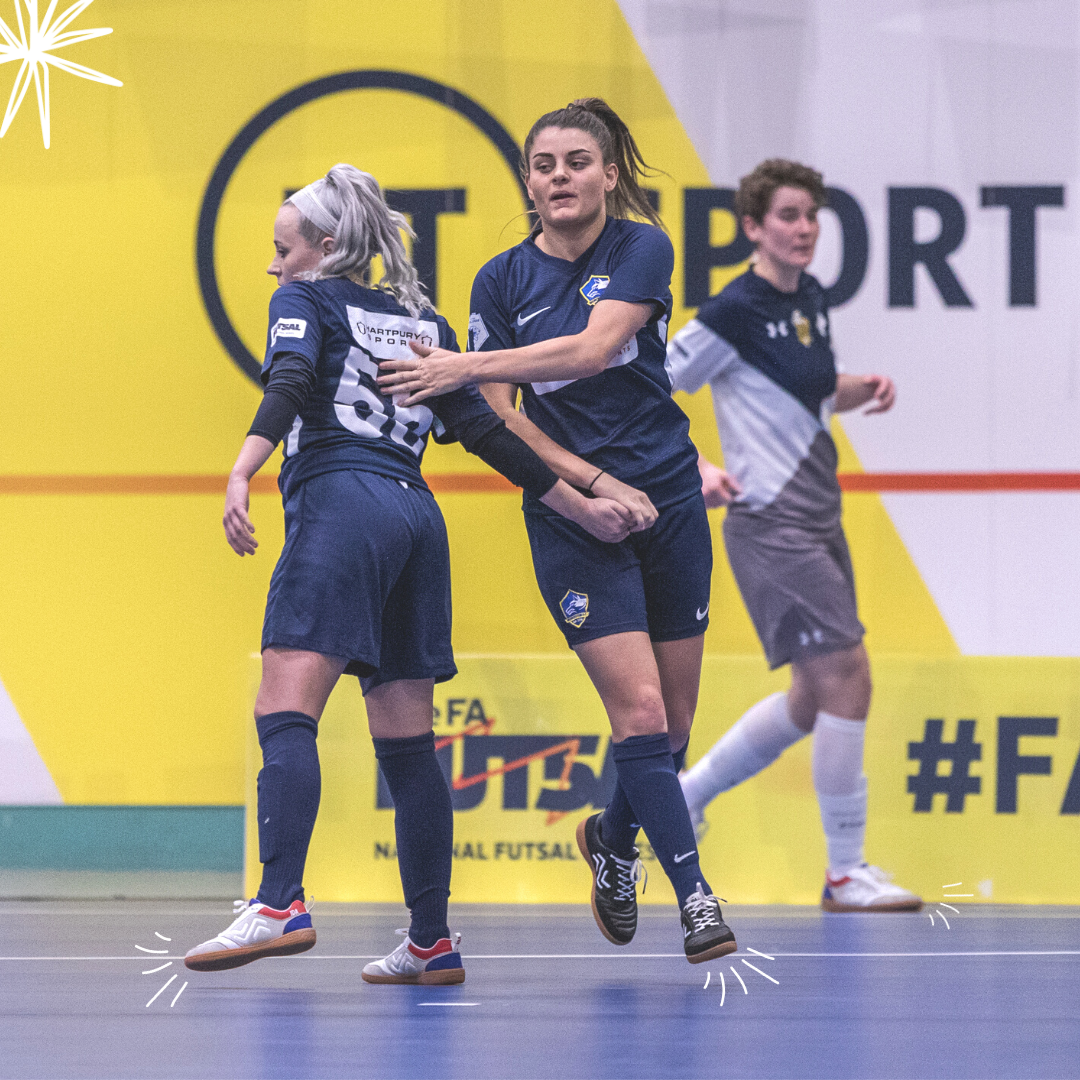 Two futsal players exchange a high five midmatch on a futsal court wearing IDA Spirit women's specific indoor futsal shoes.